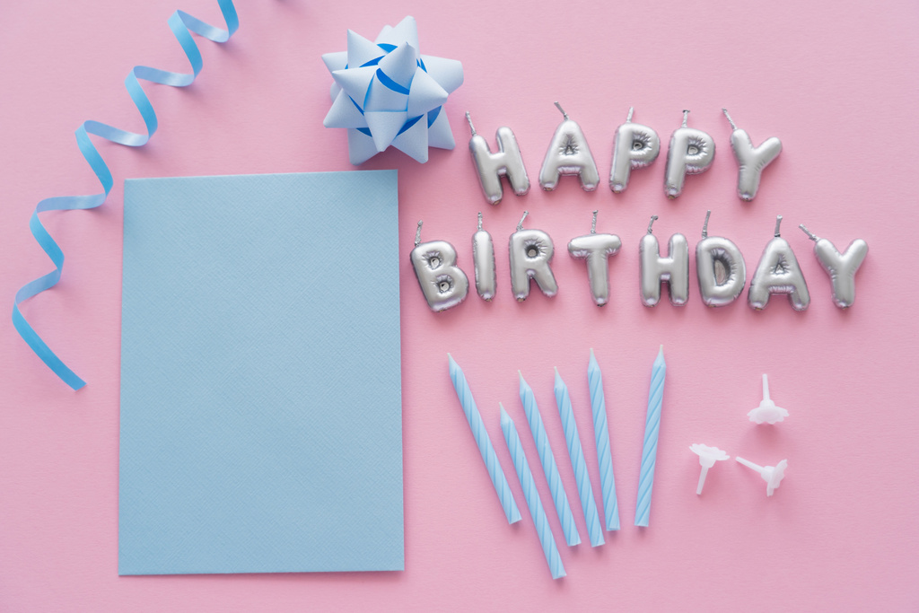 Vista superior de la tarjeta de felicitación vacía y velas en forma de letras de Feliz Cumpleaños cerca del arco de regalo sobre fondo rosa  - Foto, imagen