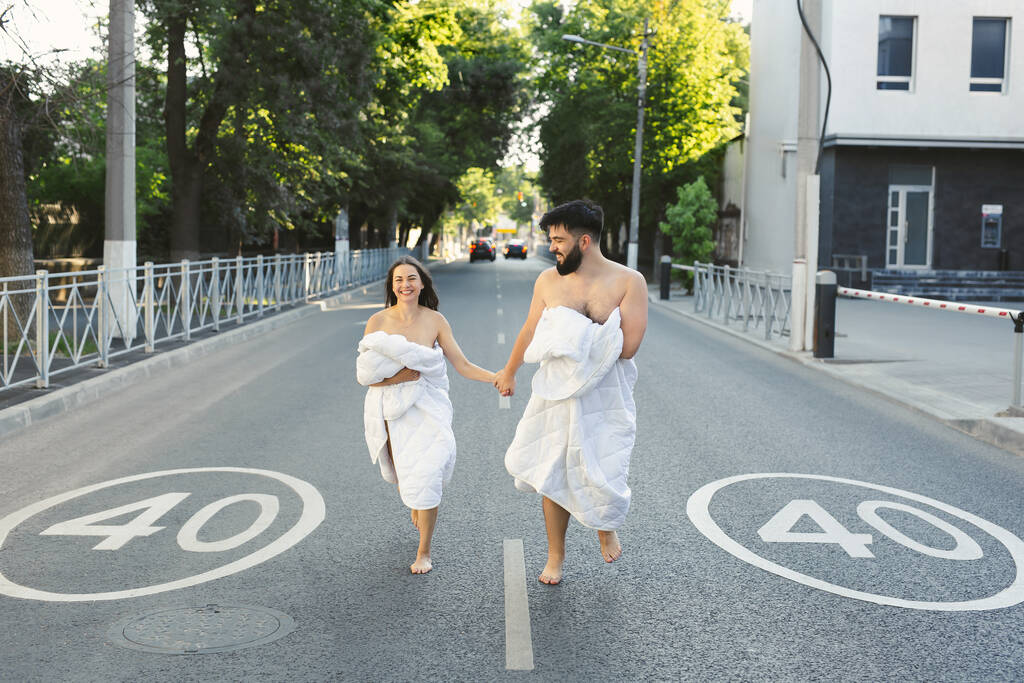 Una pareja enamorada, un hombre y una mujer, con mantas blancas, corren por el camino con mantas al amanecer.. - Foto, imagen