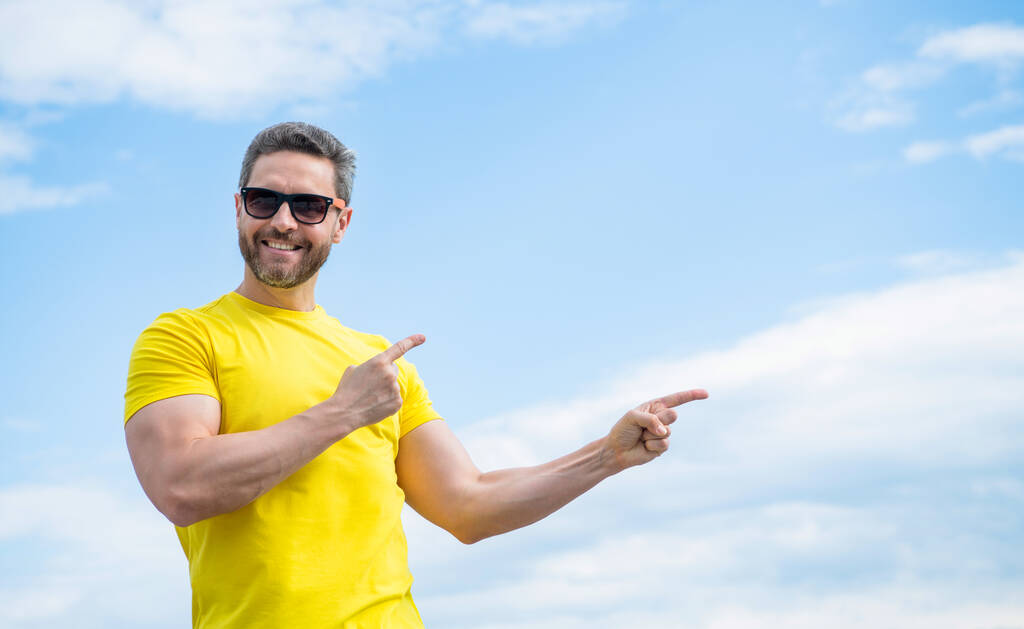 happy man in yellow shirt and sunglasses point finger on on sky background with copy space. - Photo, Image