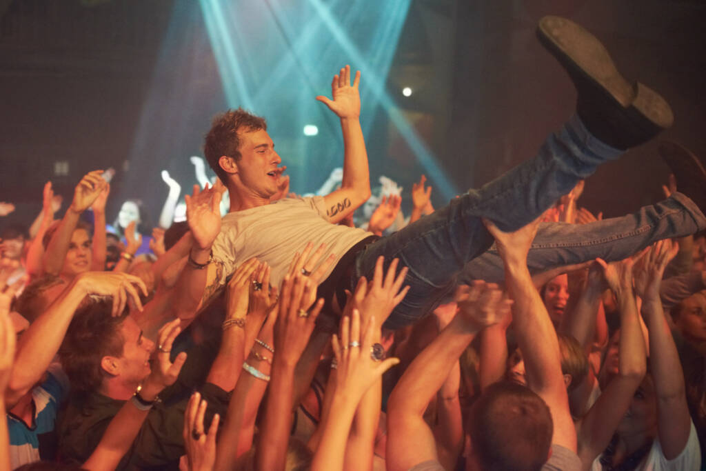 Music, party and crowd surfing with man at concert for rock, celebration and festival. Energy, light and dance with audience listening to live band show performance at disco, summer break and dj. - Photo, Image