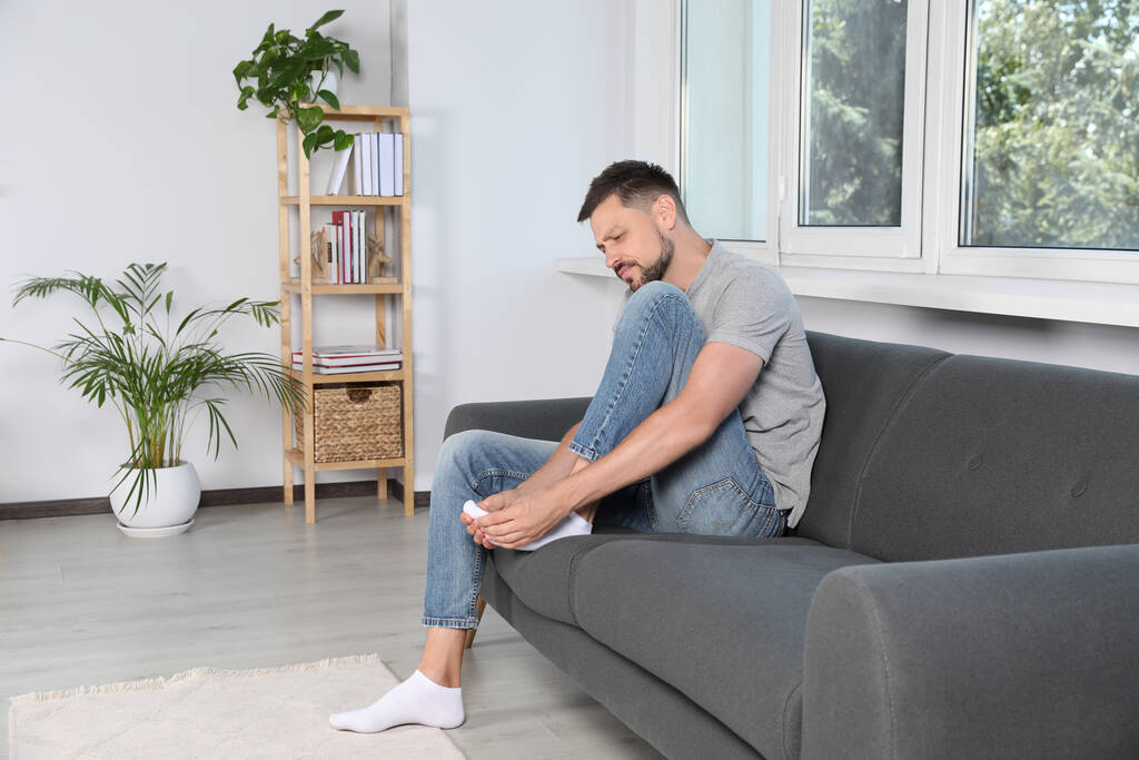 Мужчина, страдающий от болей в ногах на диване дома, место для текста - Фото, изображение