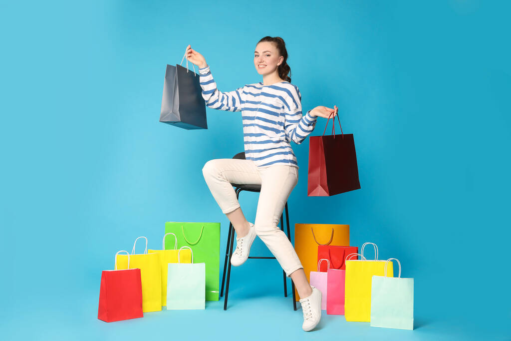 Boldog nő kezében színes bevásárló táskák széken szemben világoskék háttér - Fotó, kép
