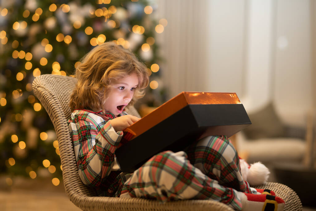Sorpresa infantil abriendo regalos de magia navideña. Niño feliz cerca del árbol de Navidad en casa - Foto, imagen