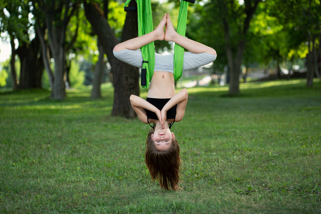 Little girl doing yoga exercises with a hammock in the park - Photo, Image