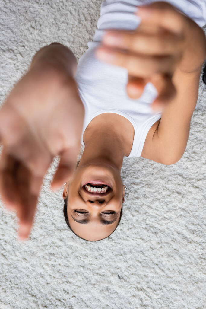 top view of positive african american woman in tank top lying on carpet  - Photo, Image
