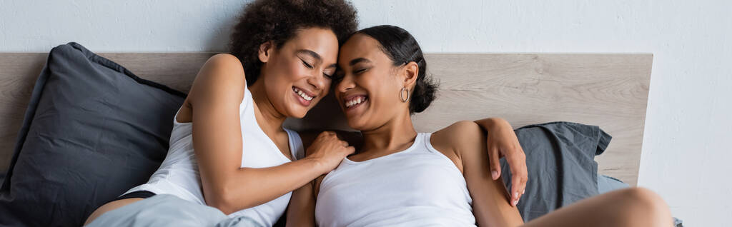 happy and lesbian african american couple with closed eyes lying on bed, banner - Photo, Image