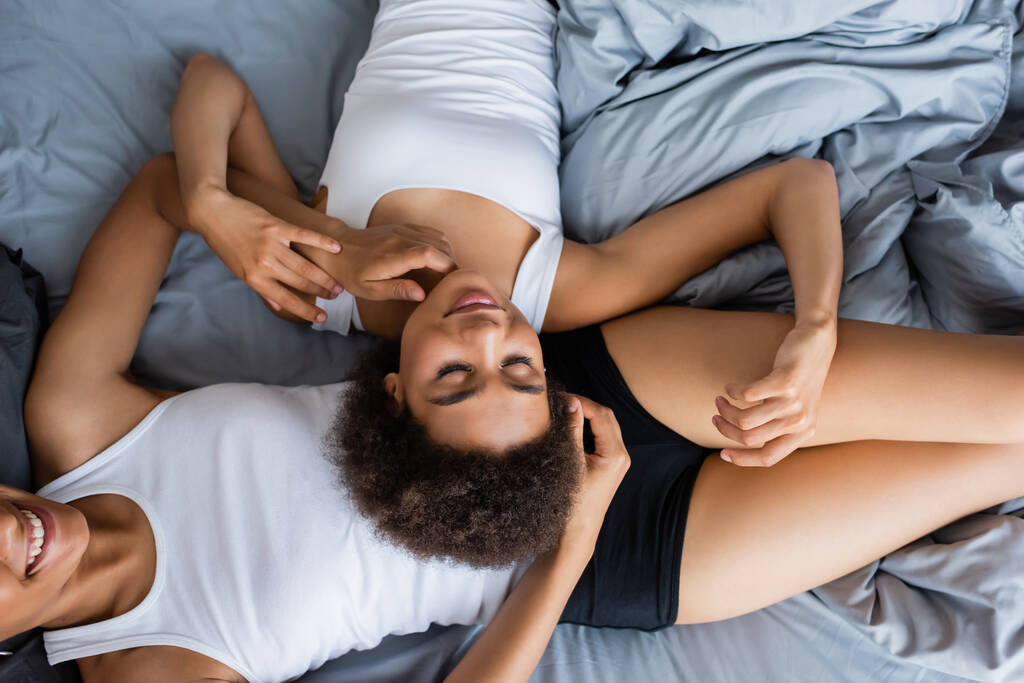 Draufsicht auf lockige Afroamerikanerin, die auf dem Bauch ihrer Freundin liegt  - Foto, Bild