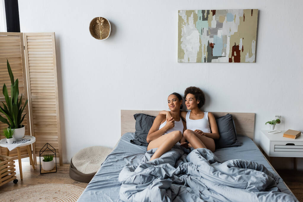 fröhliche lesbische Afroamerikanerin umarmt Freundin im modernen Schlafzimmer - Foto, Bild