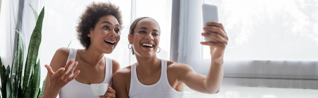 gelukkig Afrikaans amerikaans lesbisch vrouw nemen selfie met vriendin holding kopje koffie, banner - Foto, afbeelding