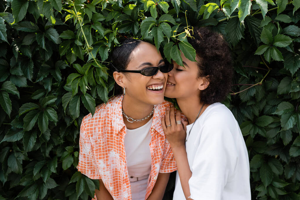 happy african american lesbian woman kissing cheek of cheerful girlfriend in sunglasses  - Photo, Image