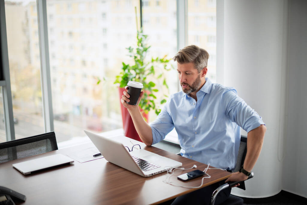 Empresário de meia-idade confiante trabalhando no escritório e usando laptop. Homem profissional bebendo café enquanto faz videoconferência no escritório. - Foto, Imagem