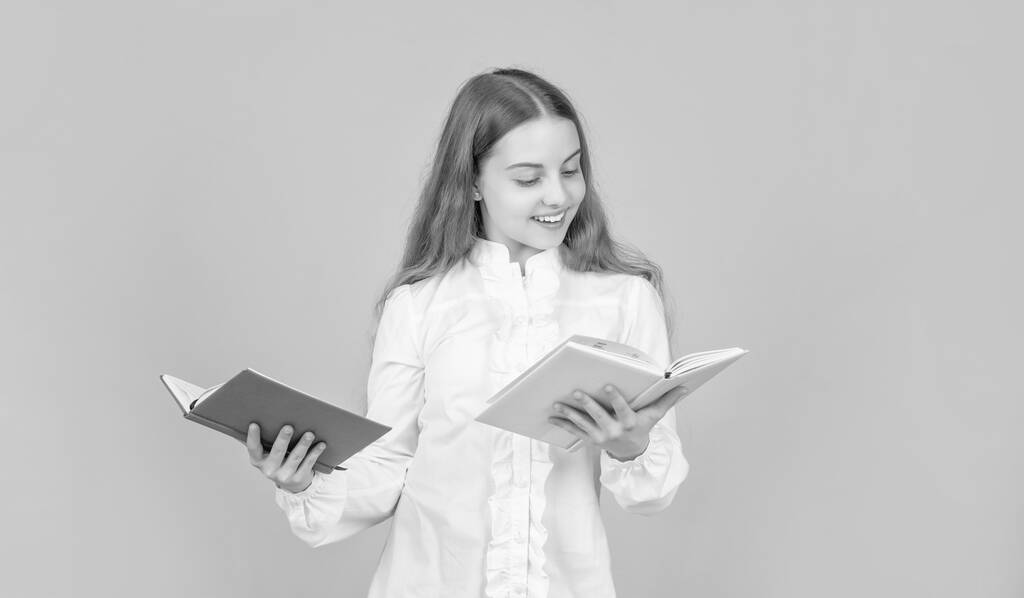 έξυπνο παιδί σε λευκό πουκάμισο έτοιμο να μελετήσει κάνει την εργασία με το βιβλίο για το κίτρινο φόντο, βιβλιοφάγος. - Φωτογραφία, εικόνα
