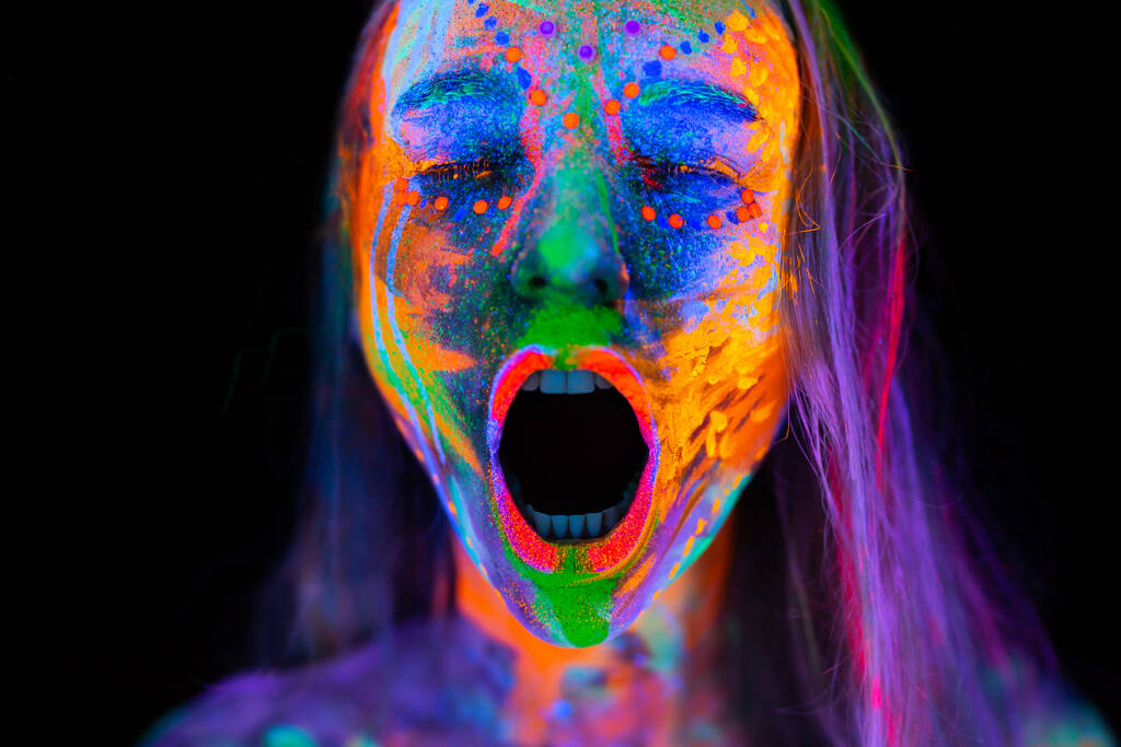 ネオンライトの美しい若い女性。UV光でポーズをとって絶叫する蛍光メイクを施したモデルのポートレート - 写真・画像