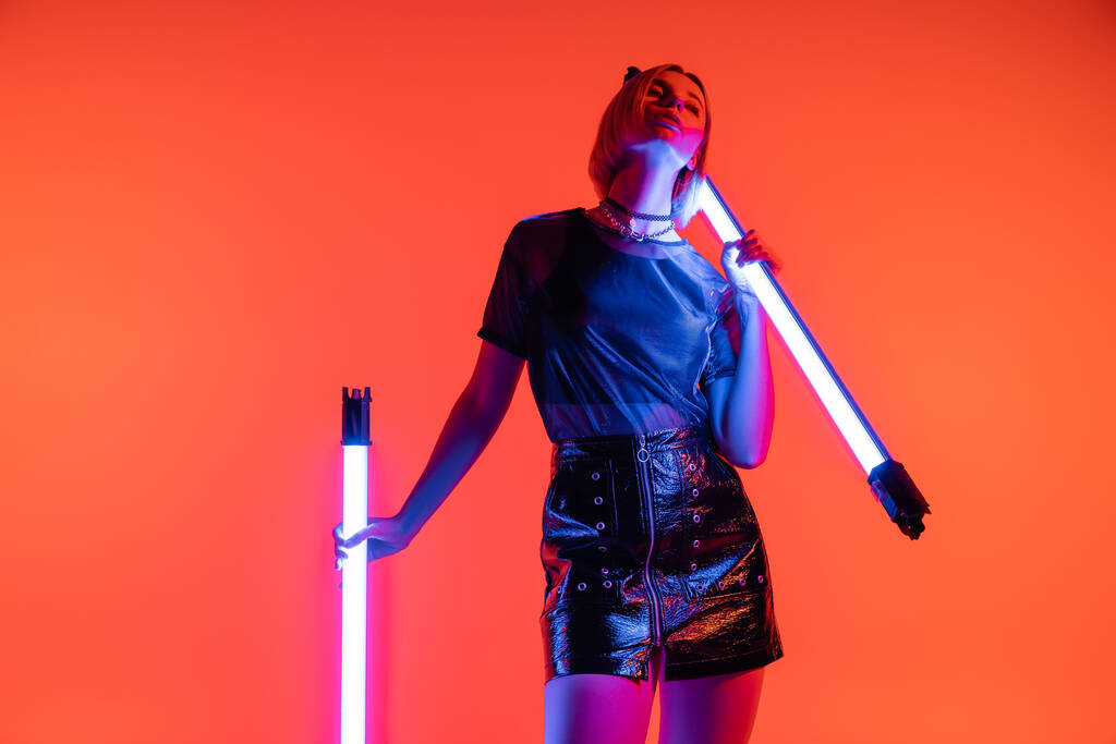 nuori nainen trendikäs t-paita ja nahka mini hame poseeraa kirkas neon lamput koralli punainen tausta - Valokuva, kuva