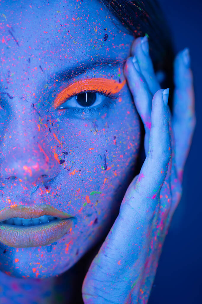 крупным планом портрет обрезанной женщины трогательное лицо с неоновым макияжем и яркие краски брызги изолированы на темно-синий - Фото, изображение