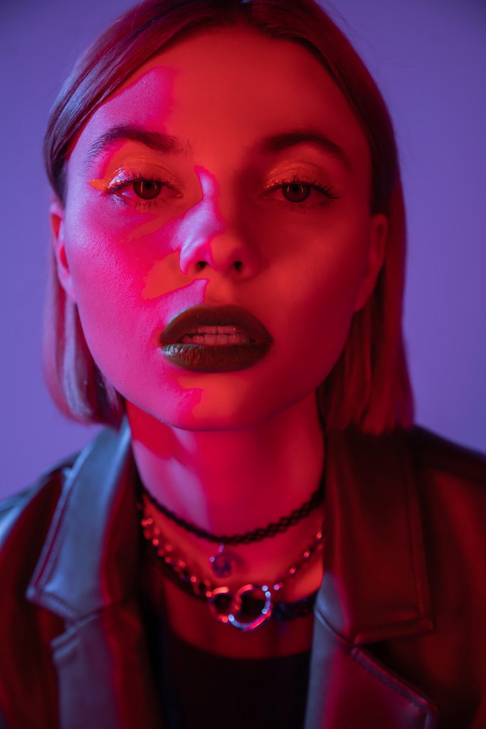 portrait of woman in bright makeup looking at camera in red light isolated on purple - Photo, Image