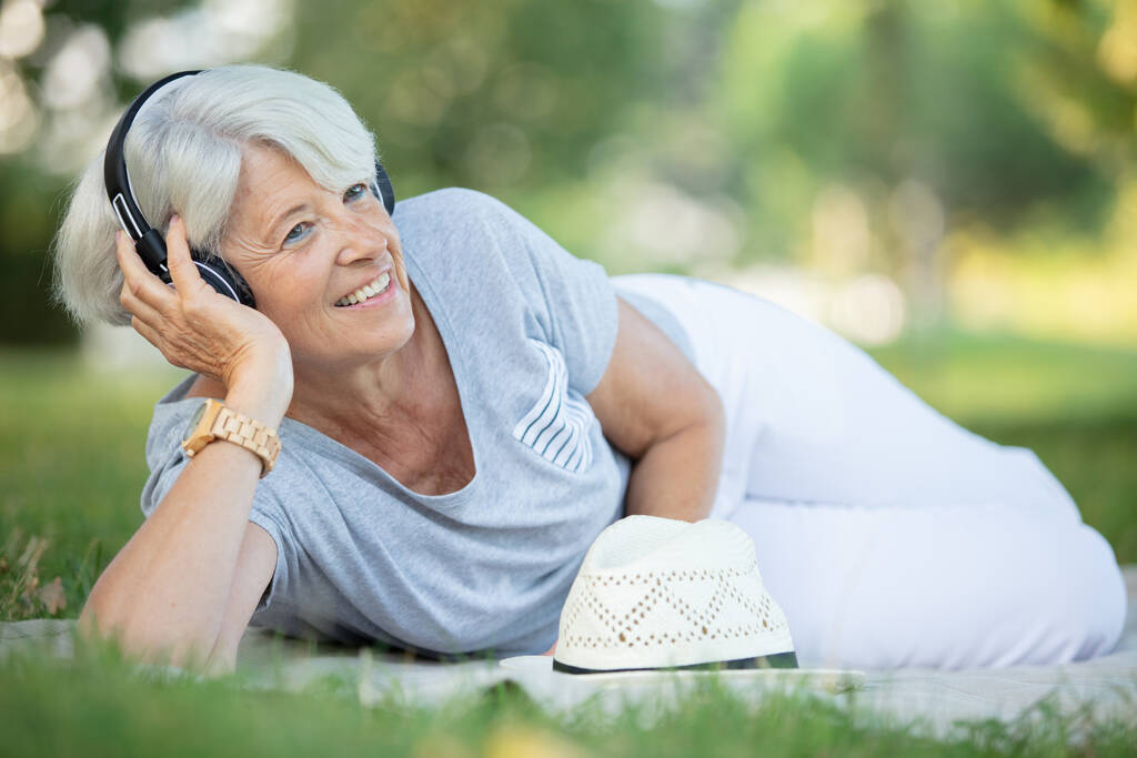 atraktivní seniorka používající sluchátka na trávě - Fotografie, Obrázek