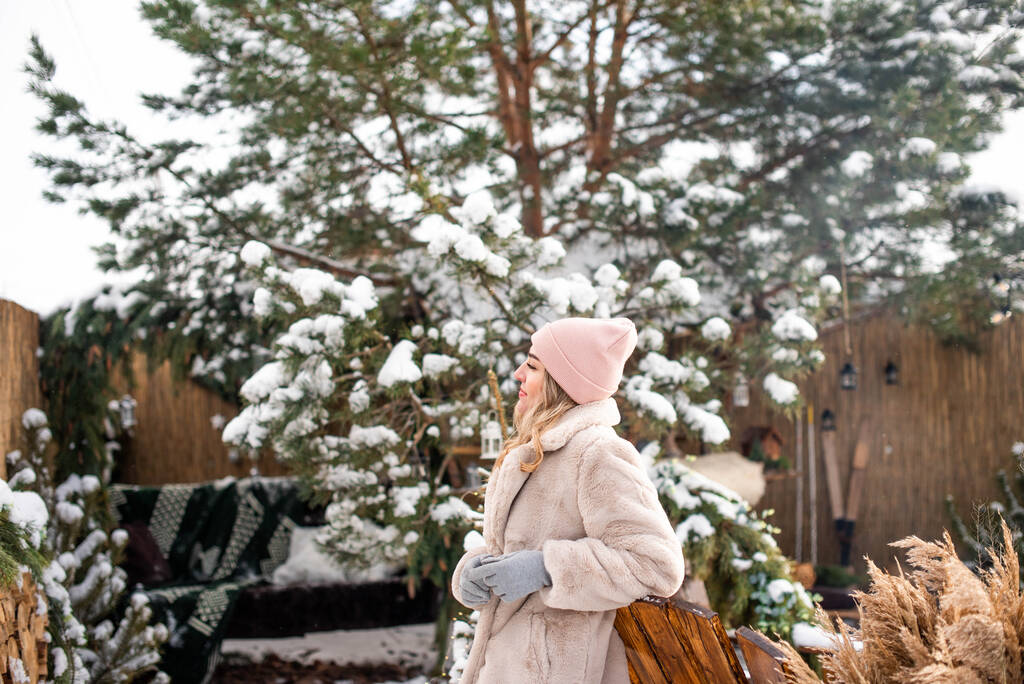 Porträt eines lächelnden hübschen Mädchens vor dem Hintergrund einer großen schneebedeckten Kiefer - Foto, Bild