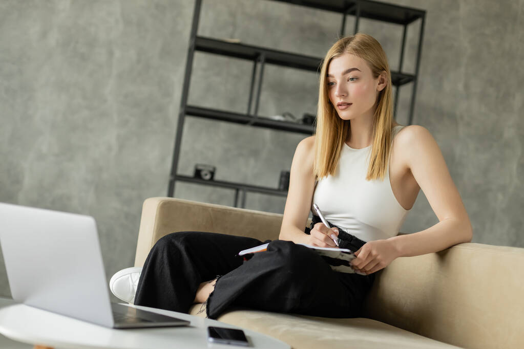 Блондинка держит ноутбук рядом с устройствами во время онлайн-обучения дома  - Фото, изображение