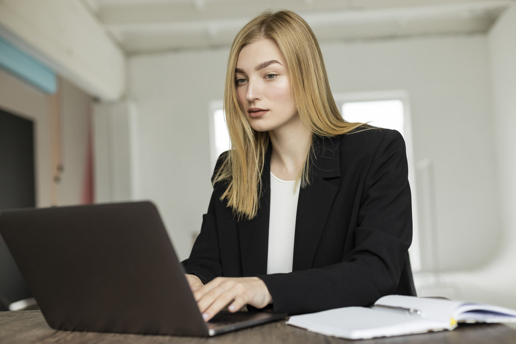 blond coach in zwart blazer typen op laptop in de buurt van notebook tijdens het werken thuis - Foto, afbeelding