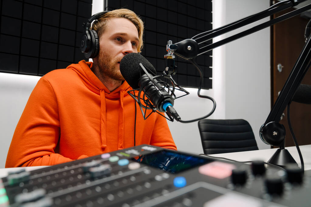 Glücklicher junger männlicher Radiomoderator mit Mikrofon und Kopfhörer während der Sendung im Studio - Foto, Bild