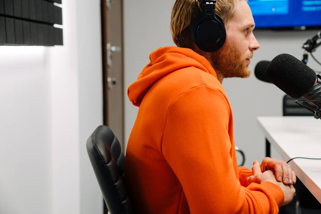 Glücklicher junger männlicher Radiomoderator mit Mikrofon und Kopfhörer während der Sendung im Studio - Foto, Bild