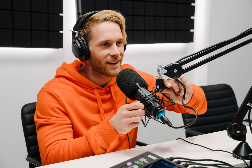 Szczęśliwy młody mężczyzna gospodarz radiowy za pomocą mikrofonu i słuchawek podczas nadawania w studio - Zdjęcie, obraz