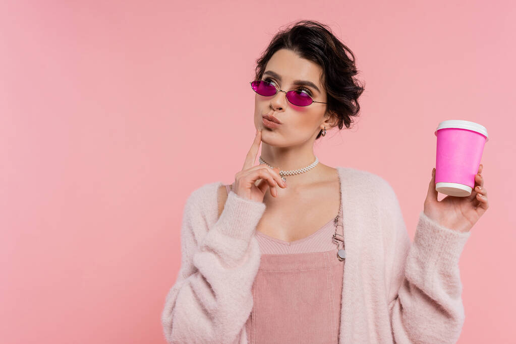 nachdenkliche Frau in trendiger Sonnenbrille mit Imbissgetränk und isoliert auf rosa - Foto, Bild