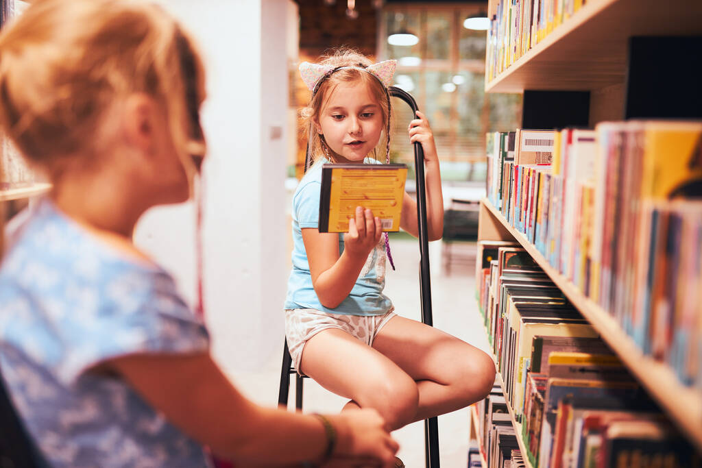 Iskoláslányok keresnek hangoskönyveket az iskolai könyvtárban. A diákok könyveket választanak. Alapfokú oktatás. Házit csinálok. Könyvekből tanulok. Vissza az iskolába. - Fotó, kép