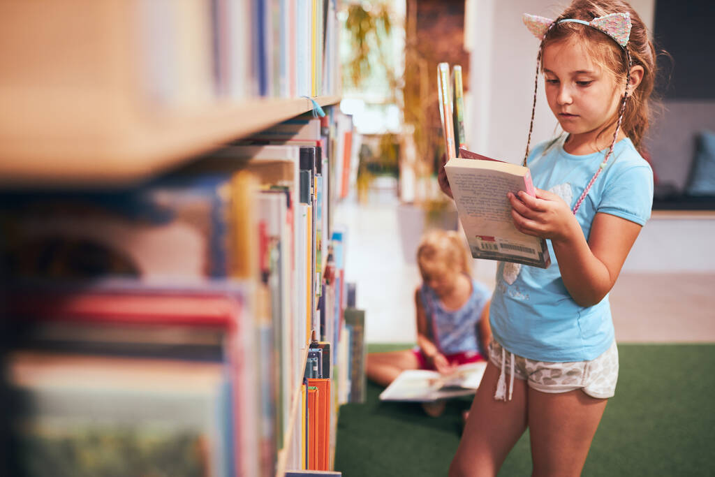 Iskoláslányok könyvet keresnek olvasásra az iskolai könyvtárban. A diákok könyveket választanak olvasásra. Könyvekből tanulok. Vissza a suliba. Alapfokú oktatás. Házit csinálok. - Fotó, kép