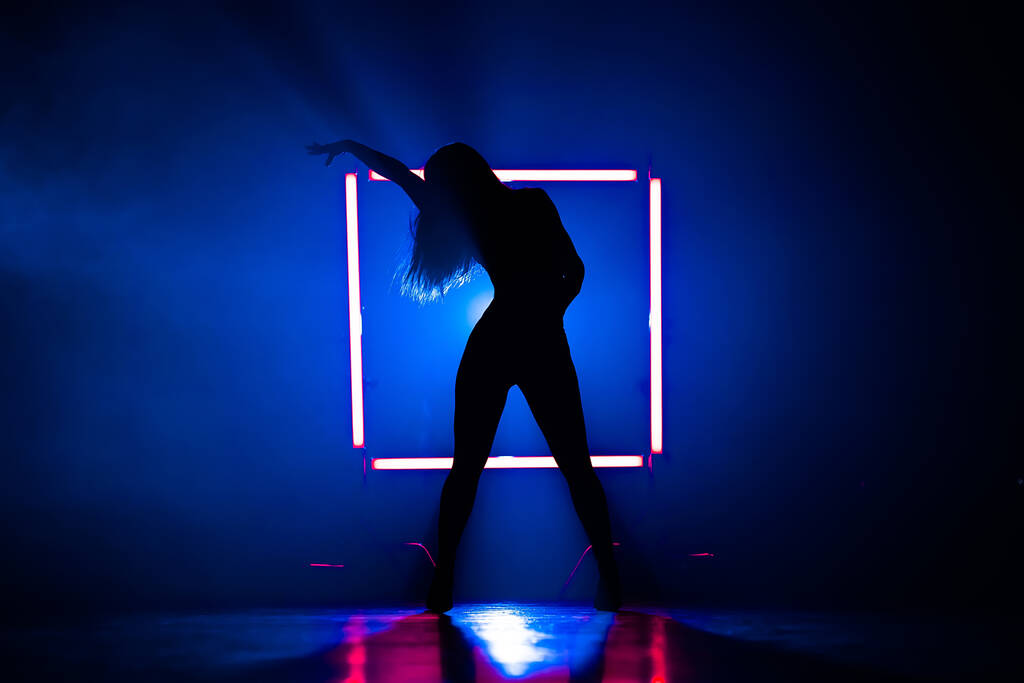 Silhouette di donna sexy che balla sulla piazza luminosa di sfondo lampade a led. Sembra seducente. Vestito sexy. Studio fumoso blu. Foto di alta qualità - Foto, immagini
