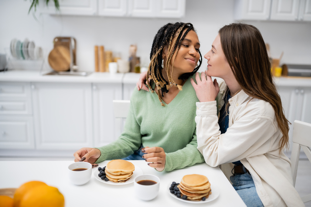 allegra donna lesbica che abbraccia la fidanzata afro-americana durante la colazione  - Foto, immagini