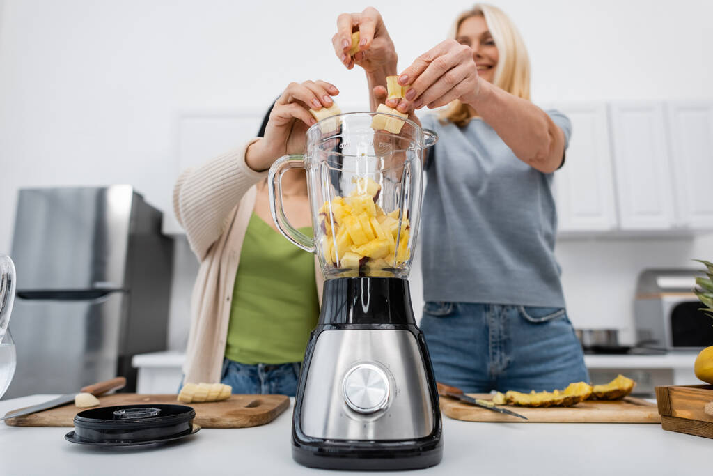 Low angle view of blurred friends putting banana in blender in kitchen  - Photo, Image