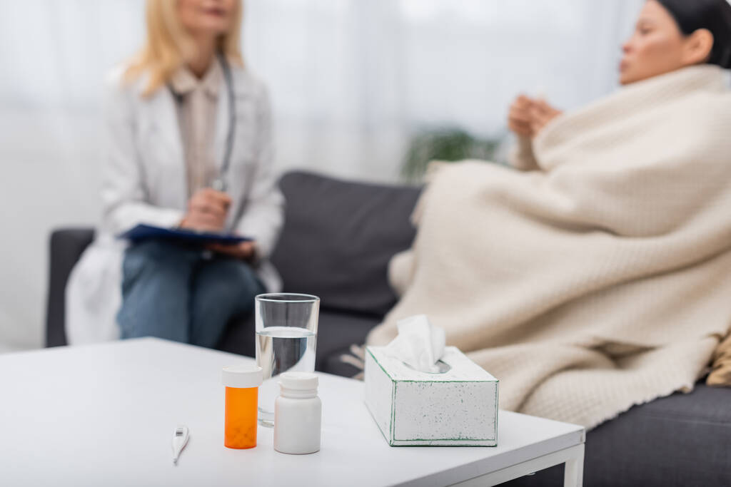 Таблетки и стакан воды возле размытой женщины и врача дома  - Фото, изображение