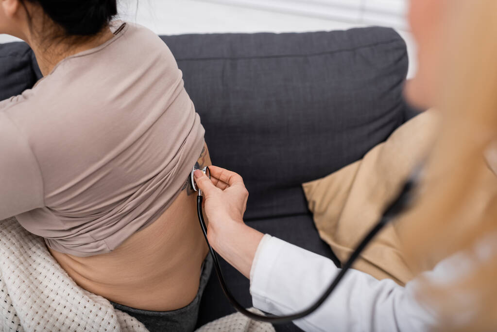 Обрезанный вид размытого доктора со стетоскопом, проверяющего спину женщины дома  - Фото, изображение