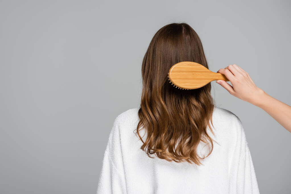 abgeschnittene Ansicht des Friseurs Bürsten glänzende und gesunde Haare der jungen Frau isoliert auf grau - Foto, Bild