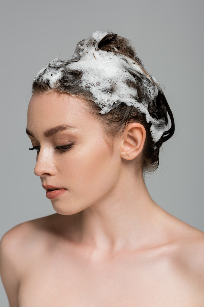 mujer joven con el pelo espumoso y húmedo aislado en gris  - Foto, Imagen