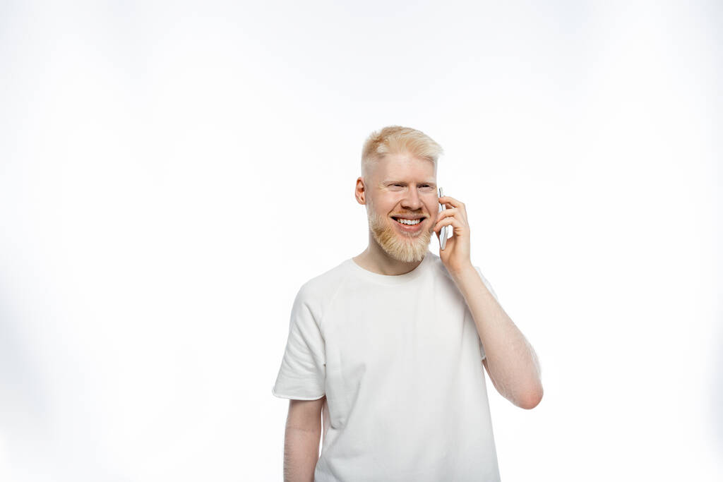 barbuto albino uomo in t-shirt parlando su smartphone e sorridendo su sfondo bianco  - Foto, immagini