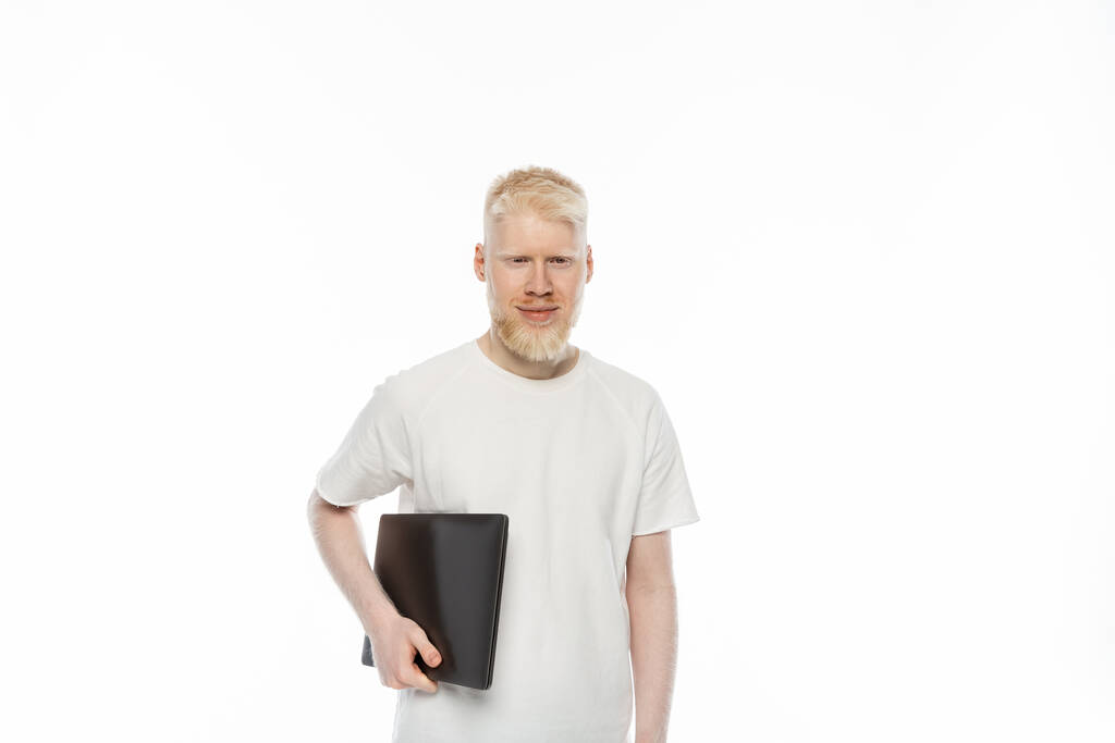 χαρούμενος Albino ελεύθερος επαγγελματίας άνθρωπος σε t-shirt κρατώντας φορητό υπολογιστή που απομονώνονται σε λευκό - Φωτογραφία, εικόνα