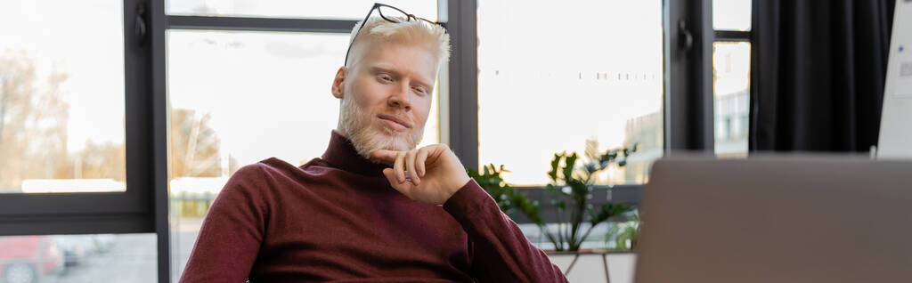 Nachdenklicher Albino-Geschäftsmann mit Brille blickt auf Laptop im Büro, Banner - Foto, Bild