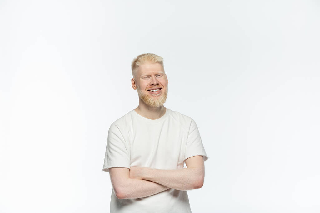 bärtiger Albino-Mann im T-Shirt, lächelnd und mit verschränkten Armen auf weißem Grund stehend  - Foto, Bild