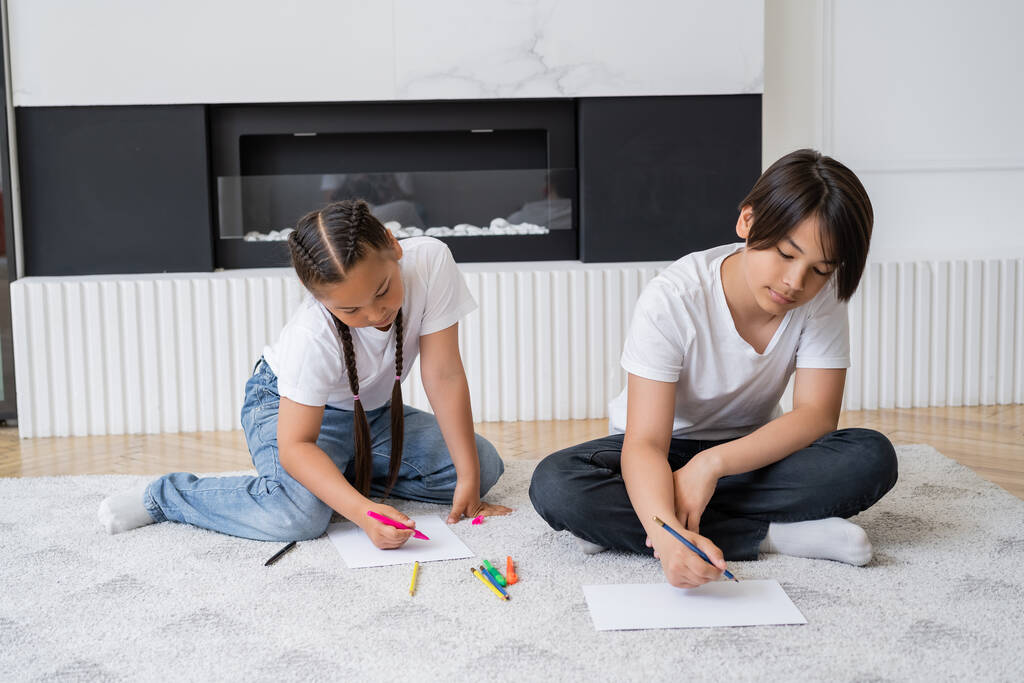 Ázsiai testvérek rajzolnak papírra szőnyegen a nappaliban  - Fotó, kép