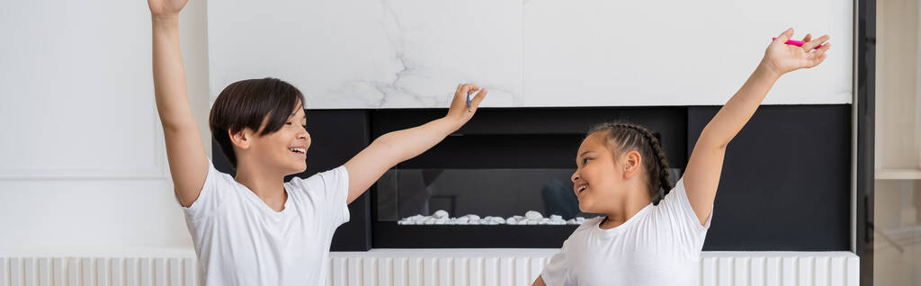 Positive asian children with raised hands looking at each other at home, banner  - Photo, Image