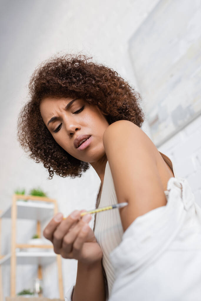 Άποψη χαμηλής γωνίας της Αφροαμερικανής γυναίκας με διαβήτη που αισθάνεται πόνο ενώ κάνει την ένεση ινσουλίνης στο σπίτι  - Φωτογραφία, εικόνα
