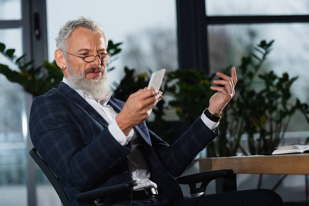 Maturo manager in occhiali da vista utilizzando smartphone in ufficio in serata  - Foto, immagini