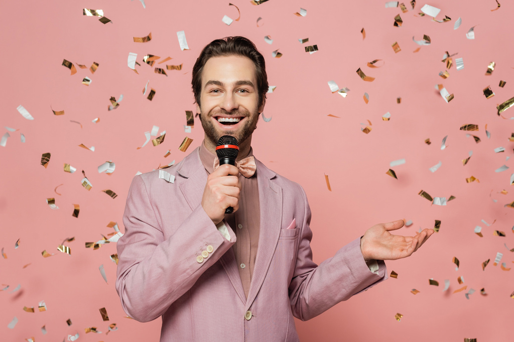 Позитивный ведущий мероприятия проведение микрофона под падение конфетти на розовый фон  - Фото, изображение