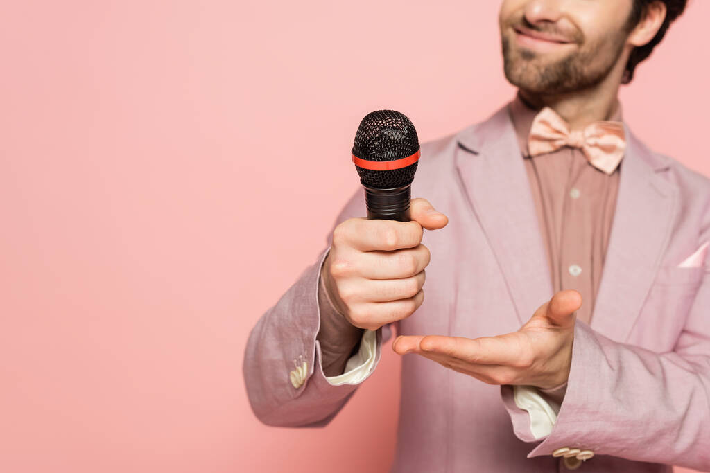 Cropped view of blurred host of event pointing at microphone isolated on pink  - Photo, Image
