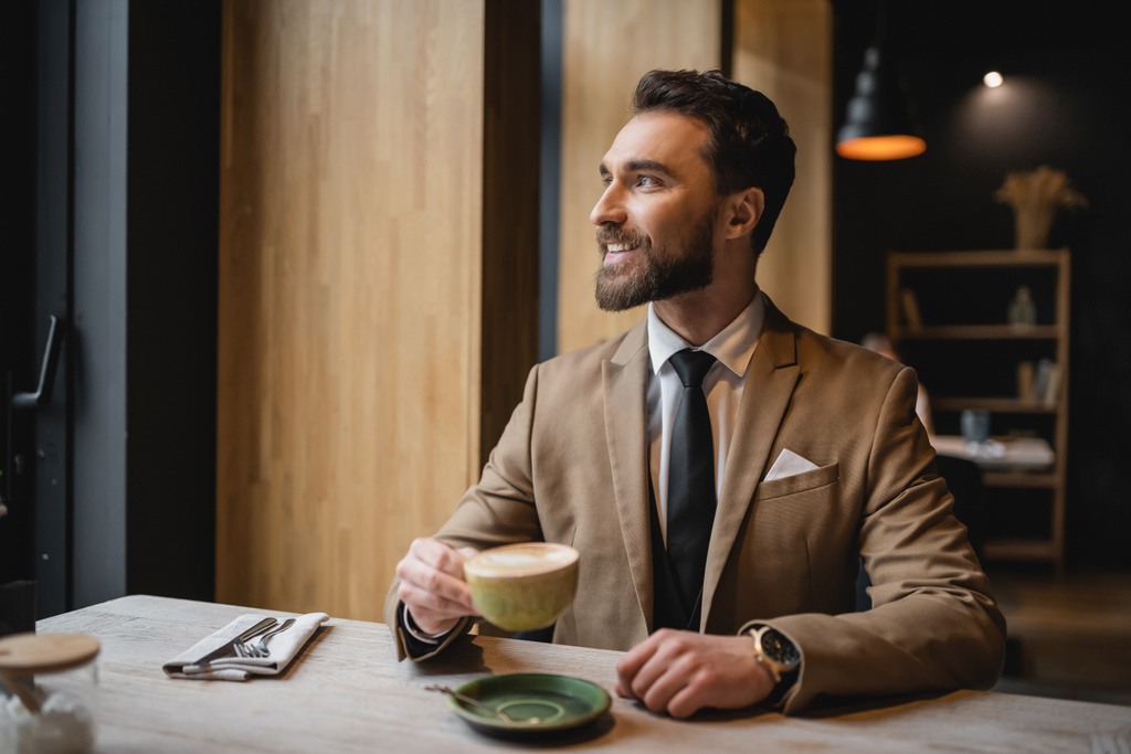 gelukkige bebaarde man in pak met een kopje cappuccino in cafe  - Foto, afbeelding