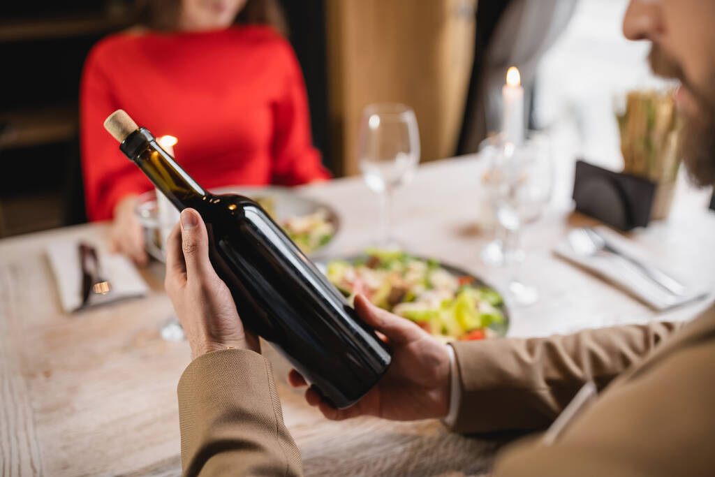 przycięty widok człowieka trzymając butelkę z winem w pobliżu dziewczyny podczas uroczystej kolacji w Walentynki - Zdjęcie, obraz