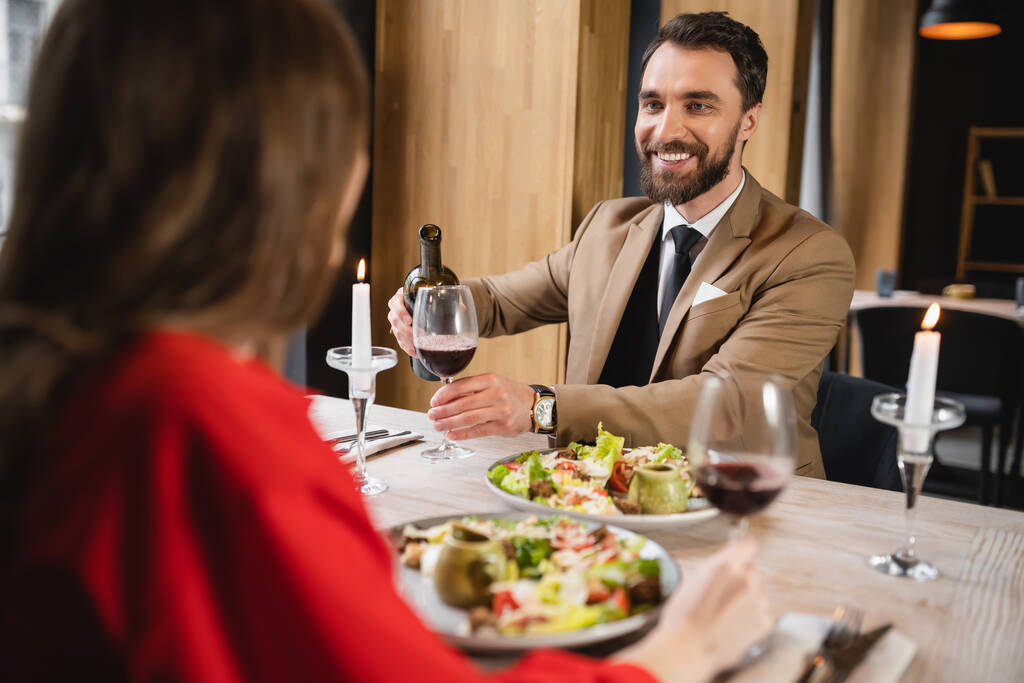 iloinen mies kaatamalla punaviiniä lasi lähellä tyttöystävä illallisen aikana Ystävänpäivä - Valokuva, kuva